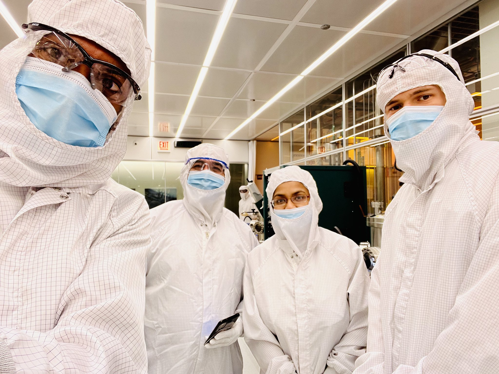Four SQMS researchers covered head-to-toe in white bunny suits with blue surgical masks.